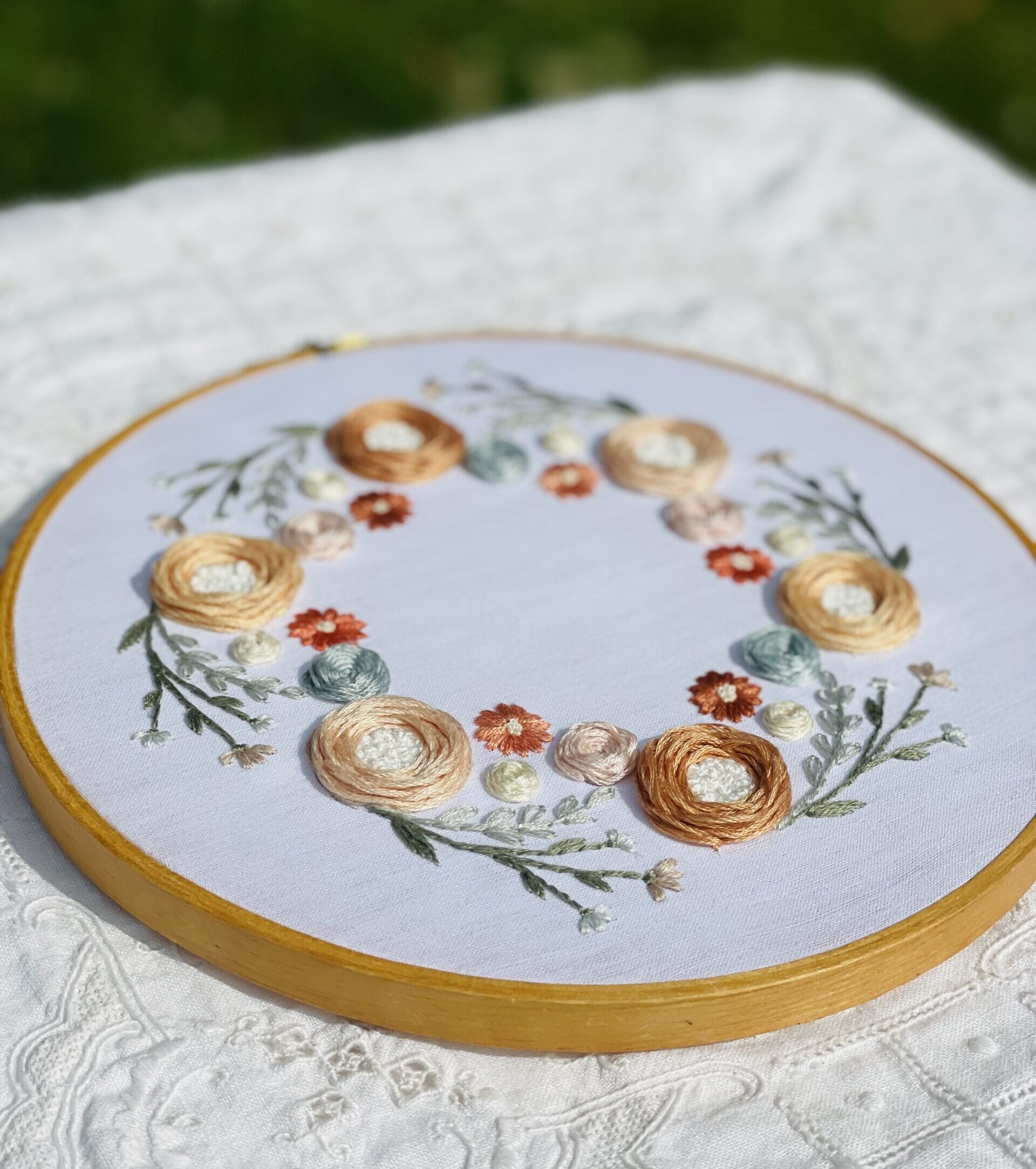 Embroidery piece with pale peach roses and light green stems, on a white cloth situated outside